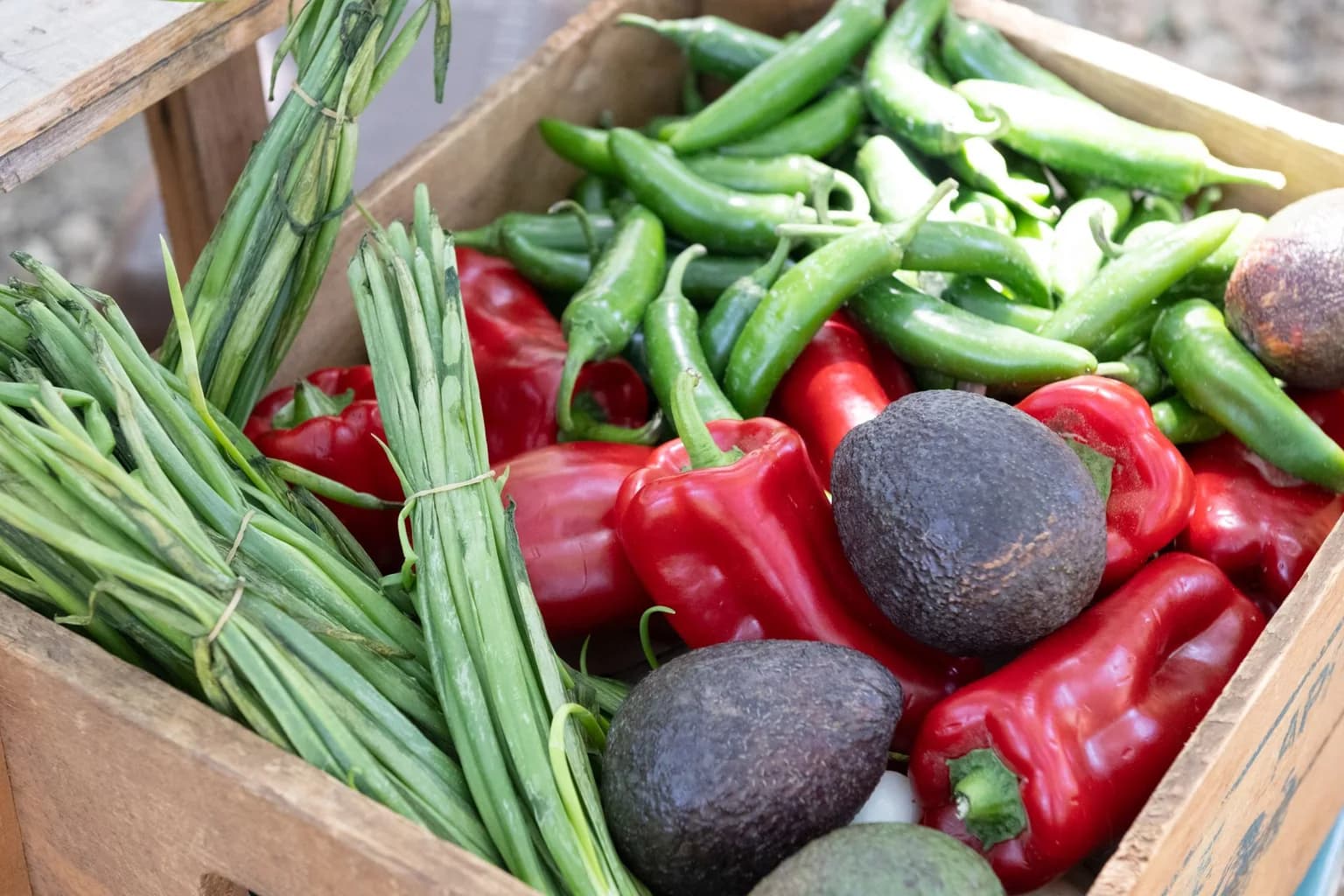 Fresh bell peppers, green beans and avocados in a wooden produce crate